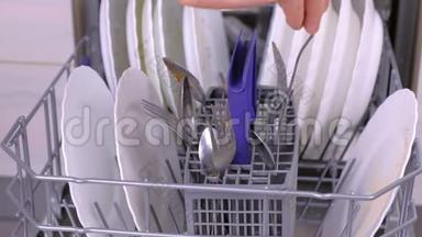 男人`手在洗碗机里放一个白色的脏盘子和勺子，然后在厨房里运行。